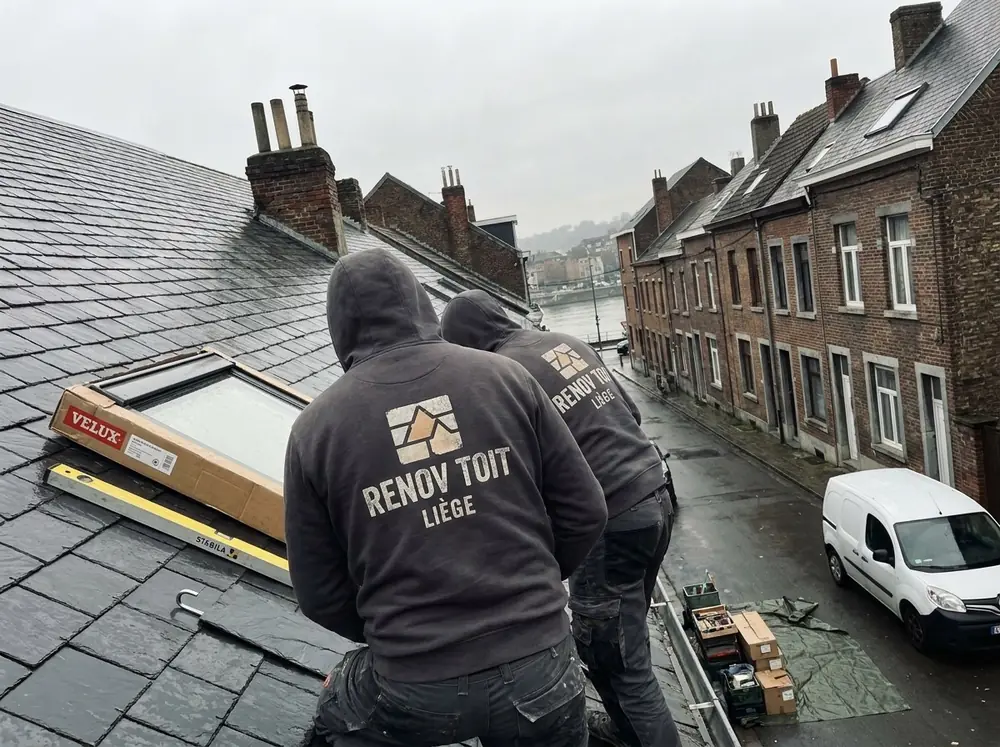 Deux couvreurs Renov'Toit Liège posant une fenêtre de toit dans une toiture en ardoises